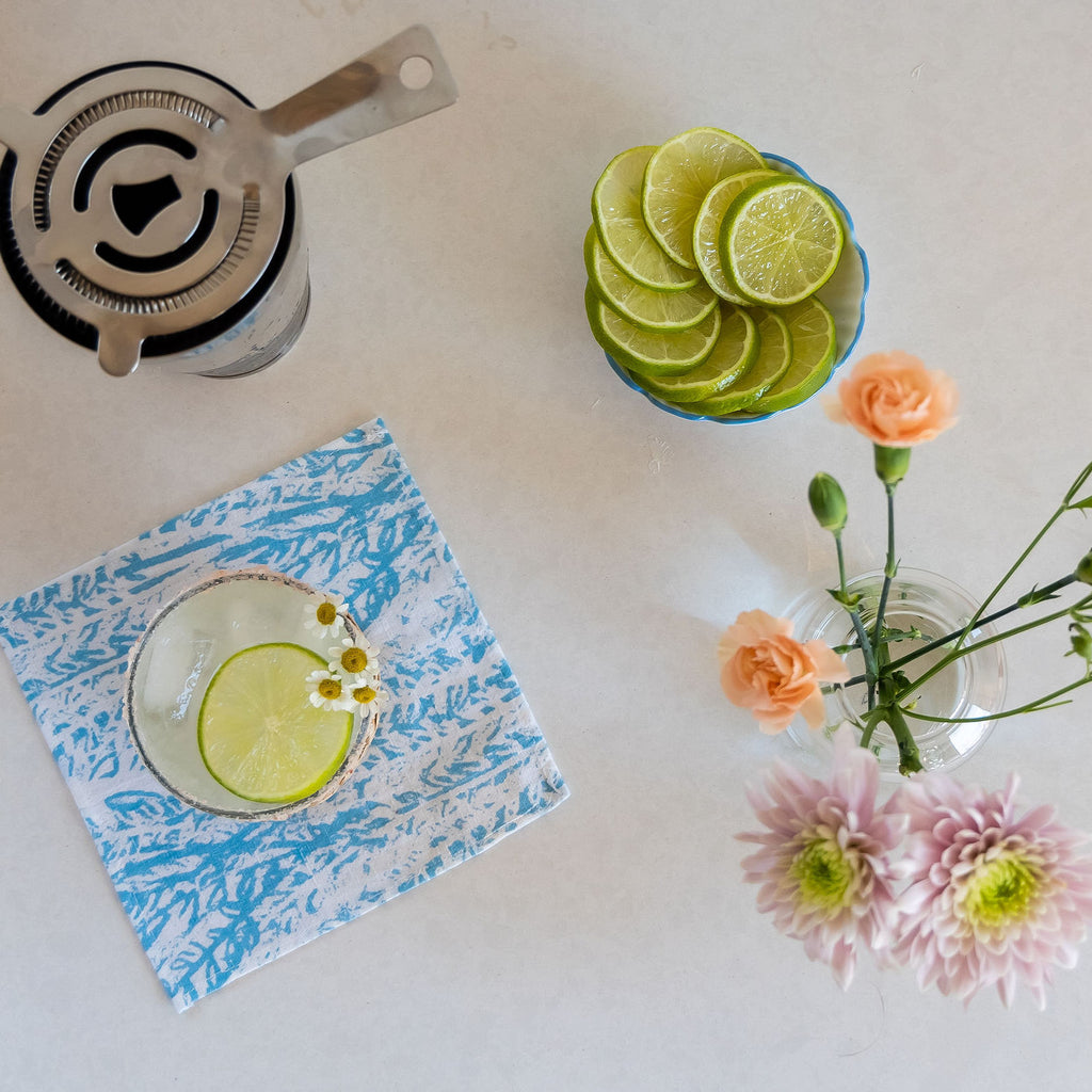 Cocktail atop a Laguna napkin featuring foliage hues, complented with vibrant flowers.