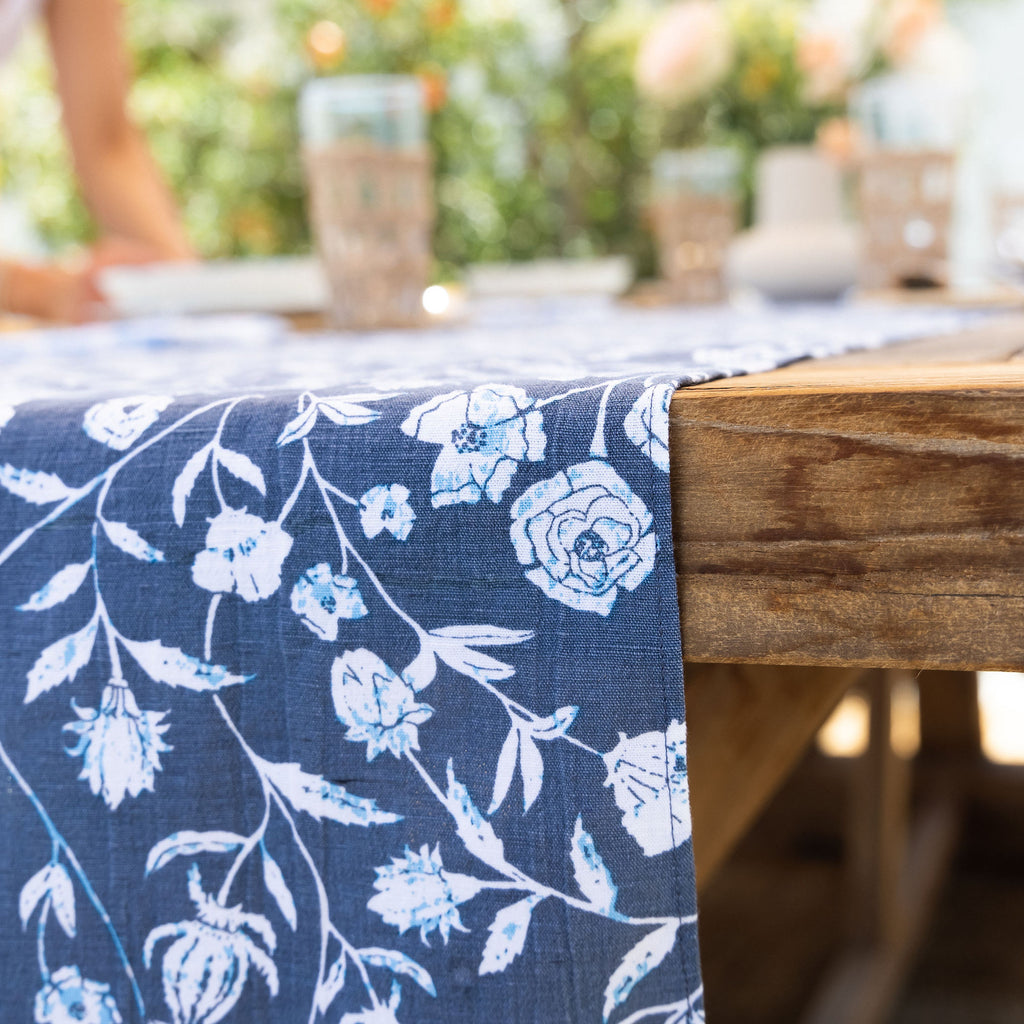 Floral patterns, uniquely printed, complement a wooden tablre. The Montecito Table Runner is the perfect addition to any occasion.