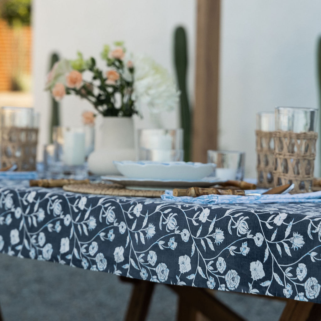 This dinner setting features the Montecito Tabecloth in blue and white floral patterns. A vase of flowers sits atop the tablecloth as the perfect detail to a vibrant gathering.